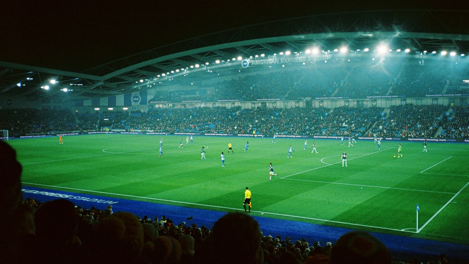A floodlit football stadium at night with pitch-side perimeter advertising boards
